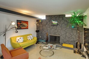 Una sala de estar con una pared de piedra, un sofá amarillo, una mesa de centro de vidrio y una chimenea.