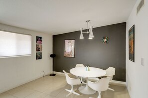 A modern dining area with a round table and white chairs, a floor lamp, and wall art including a poster and a clock.