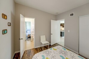 Un dormitorio con cama, una silla y un baño visible a través de una puerta abierta.