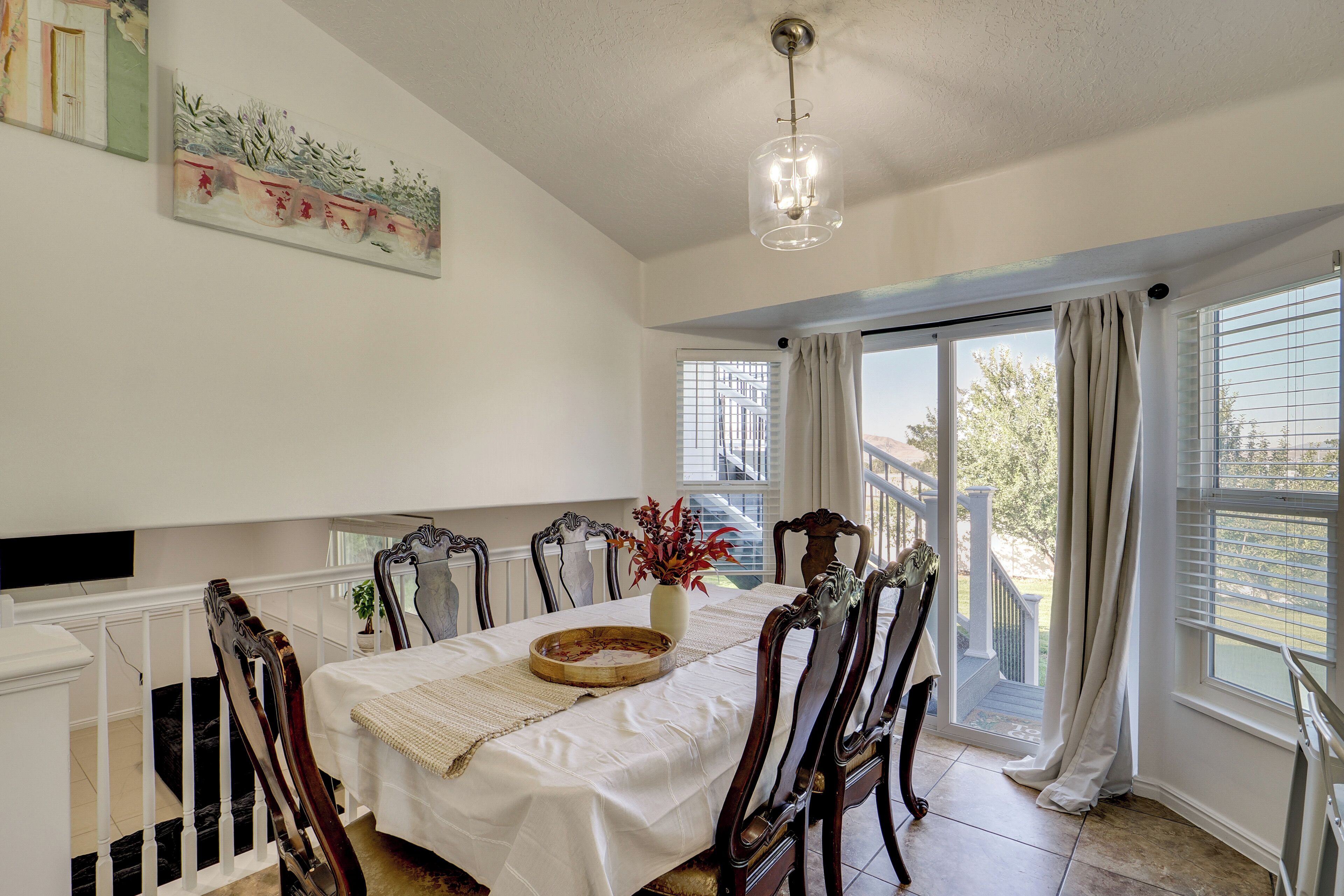 A dining room with a table set for four, chairs, a vase with flowers, and a ceiling light fixture.