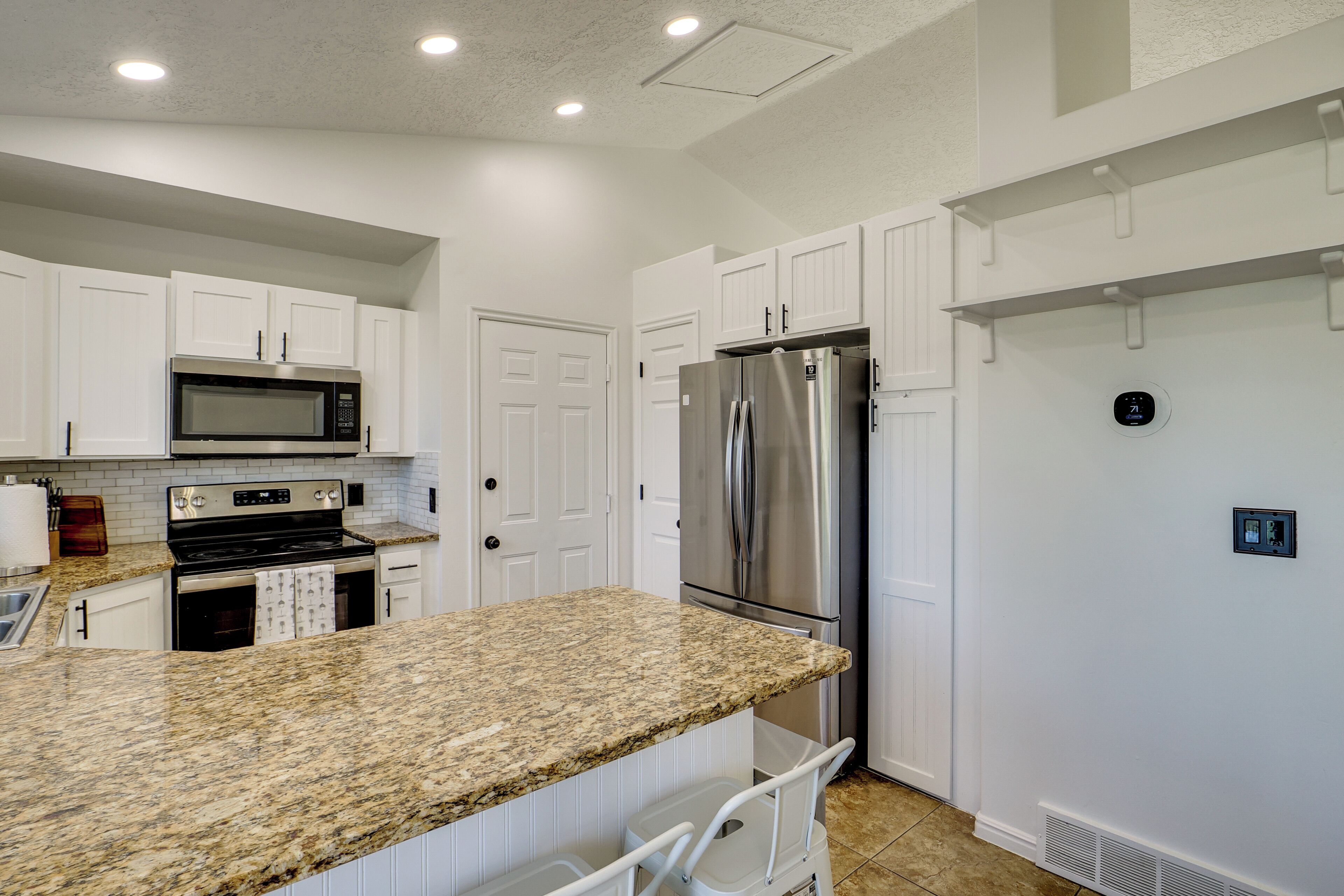 A kitchen with white cabinets, a stainless steel refrigerator, a microwave, and a granite countertop.