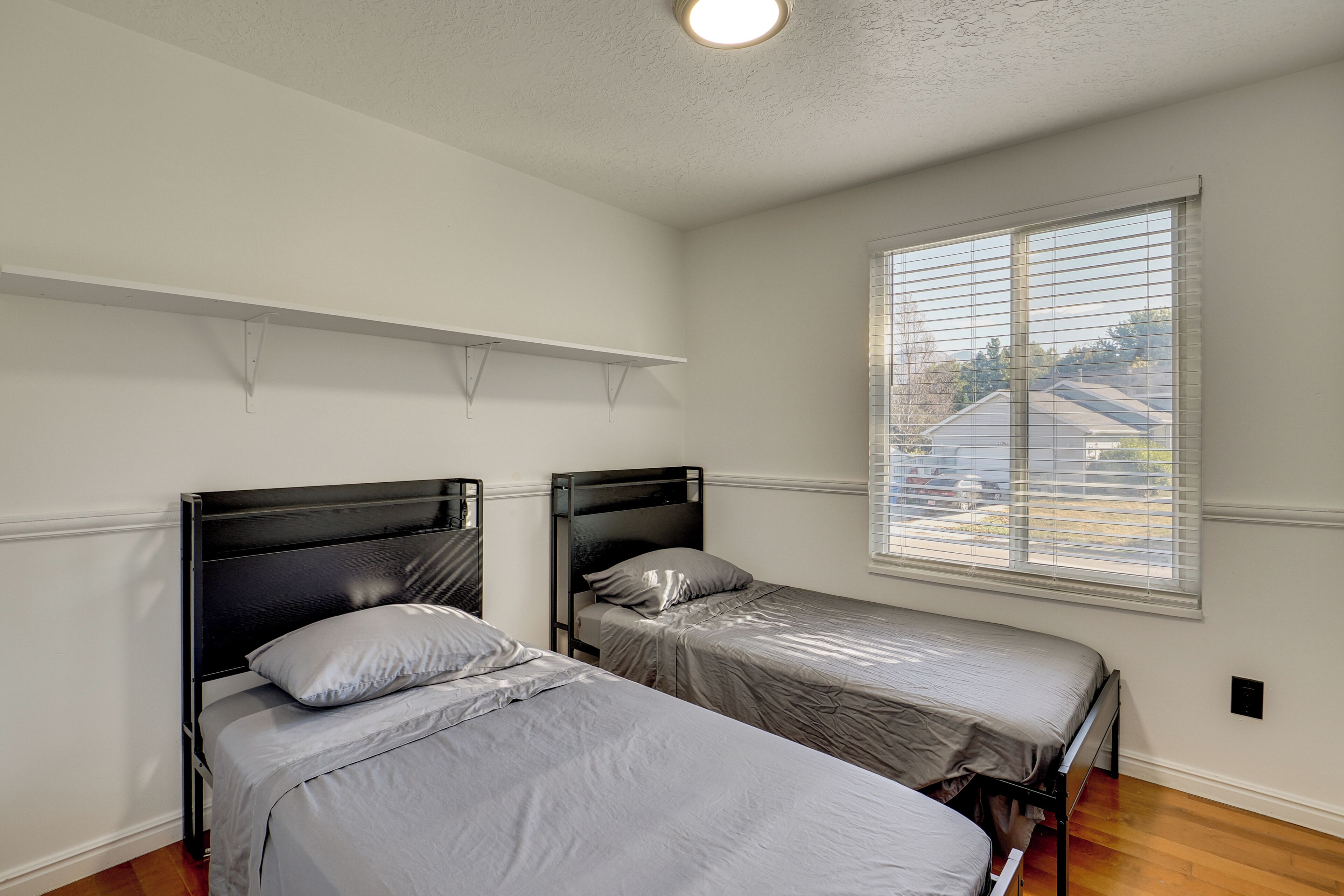 Un dormitorio con dos camas individuales, una ventana con persianas y una lámpara en el techo.
