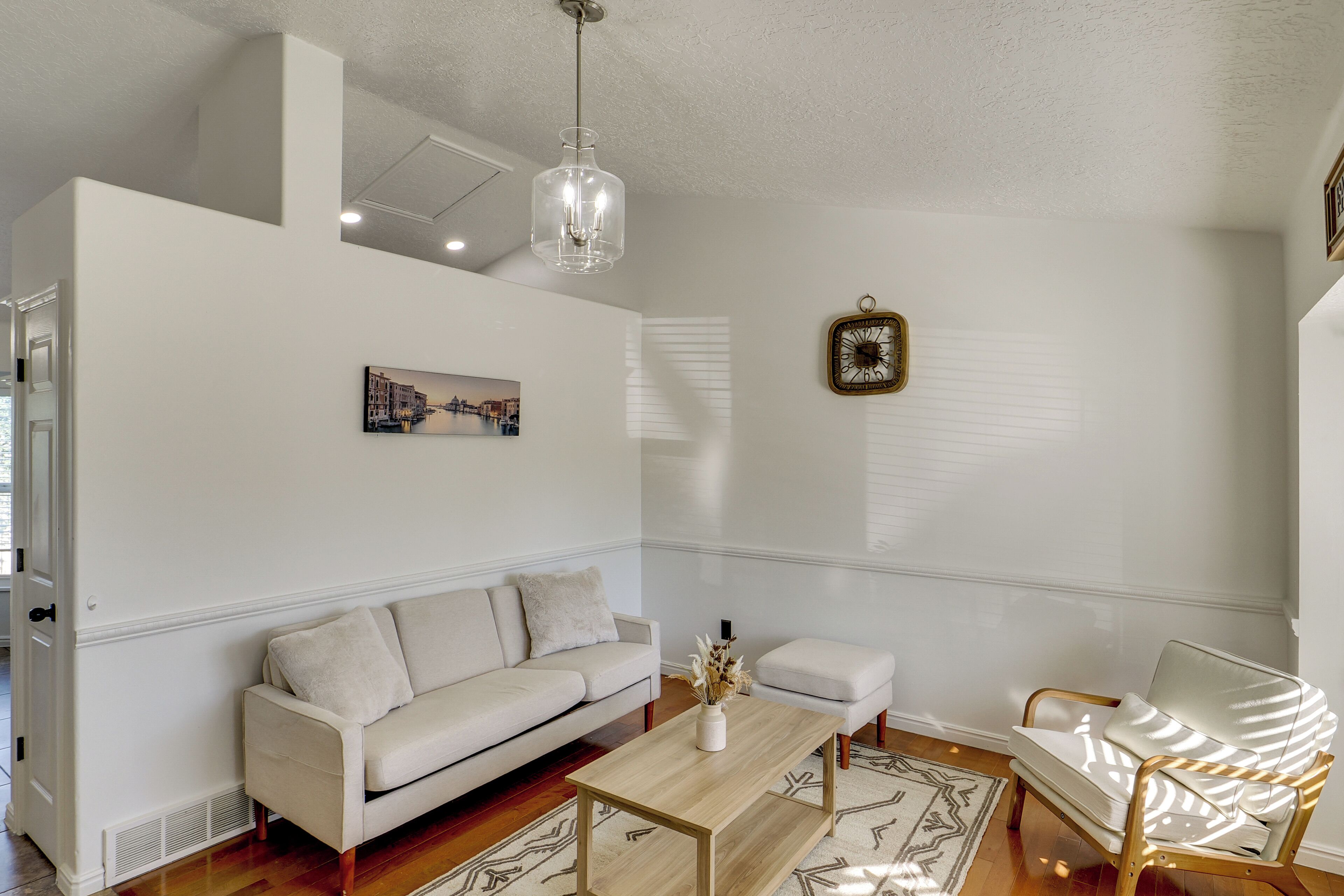 A living room with a white sofa, a wooden coffee table, a white armchair, and a hanging light fixture.