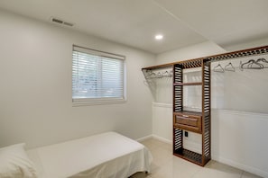 Un dormitorio con cama individual, ventana con persianas, armario con espejo y rejilla en el techo.