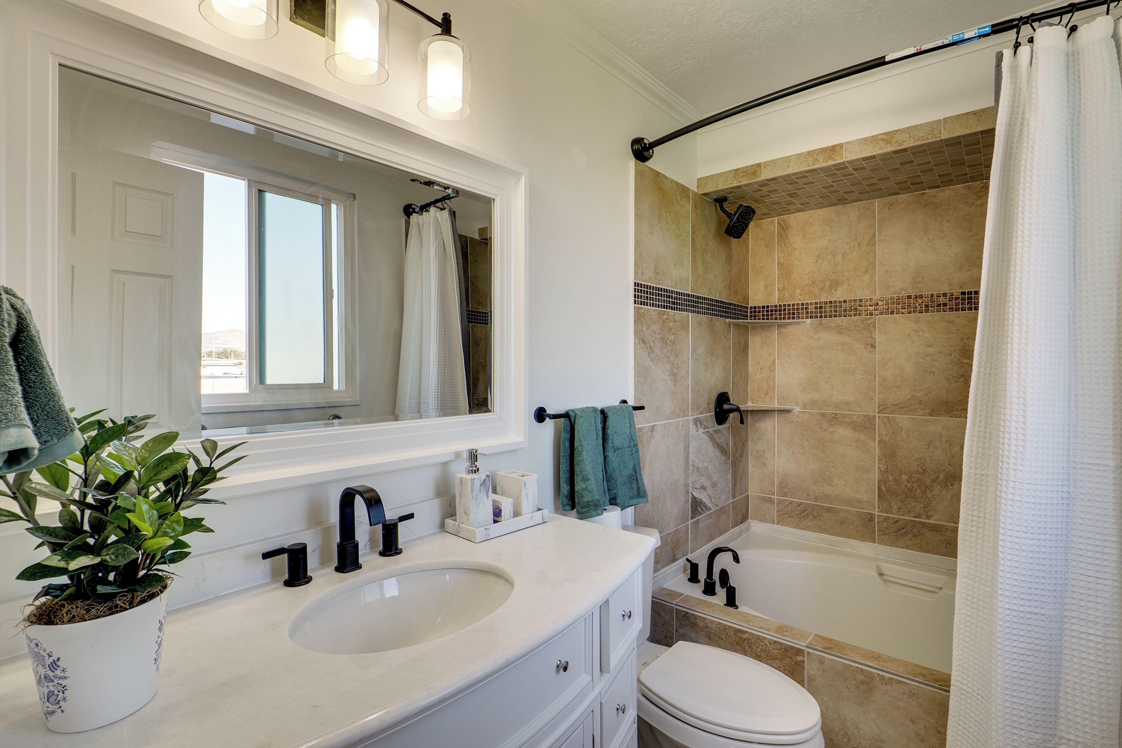 Une salle de bain avec un lavabo blanc, un miroir, un porte-serviettes, des toilettes et une douche avec un mur recouvert de carreaux beiges.