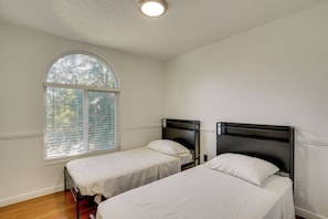 Una habitación con dos camas, un amplio ventanal de arco y una lámpara en el techo.