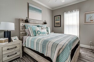 Un dormitorio con cama, mesita de noche, lámpara y una obra de arte.