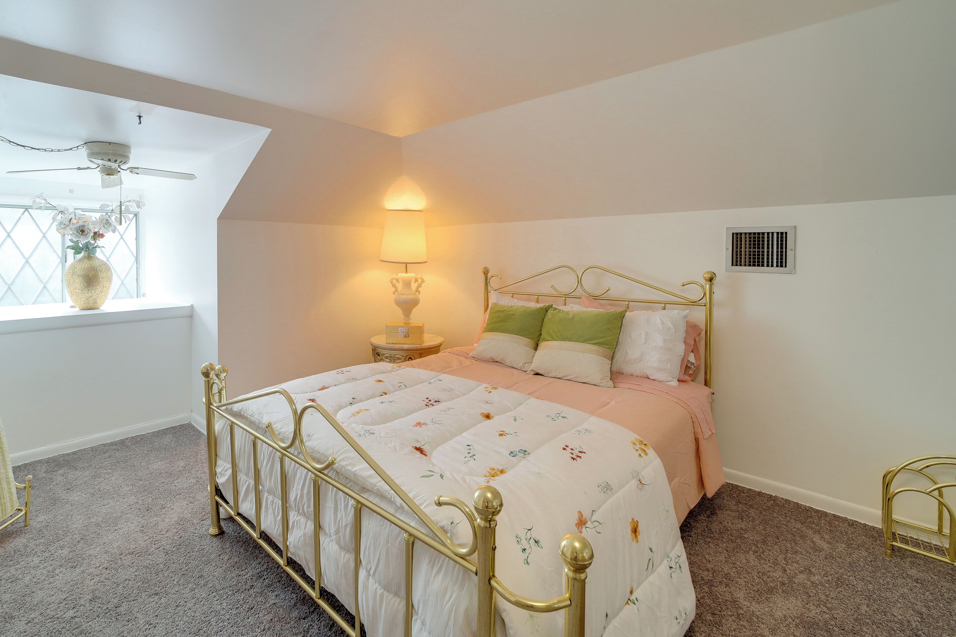 A bedroom with a bed, a nightstand, a lamp, a window with a view, and a ceiling fan.
