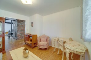 Una sala de estar con chimenea de ladrillo, un mueble de madera, un sillón tapizado en rosa y una mesa de mármol.