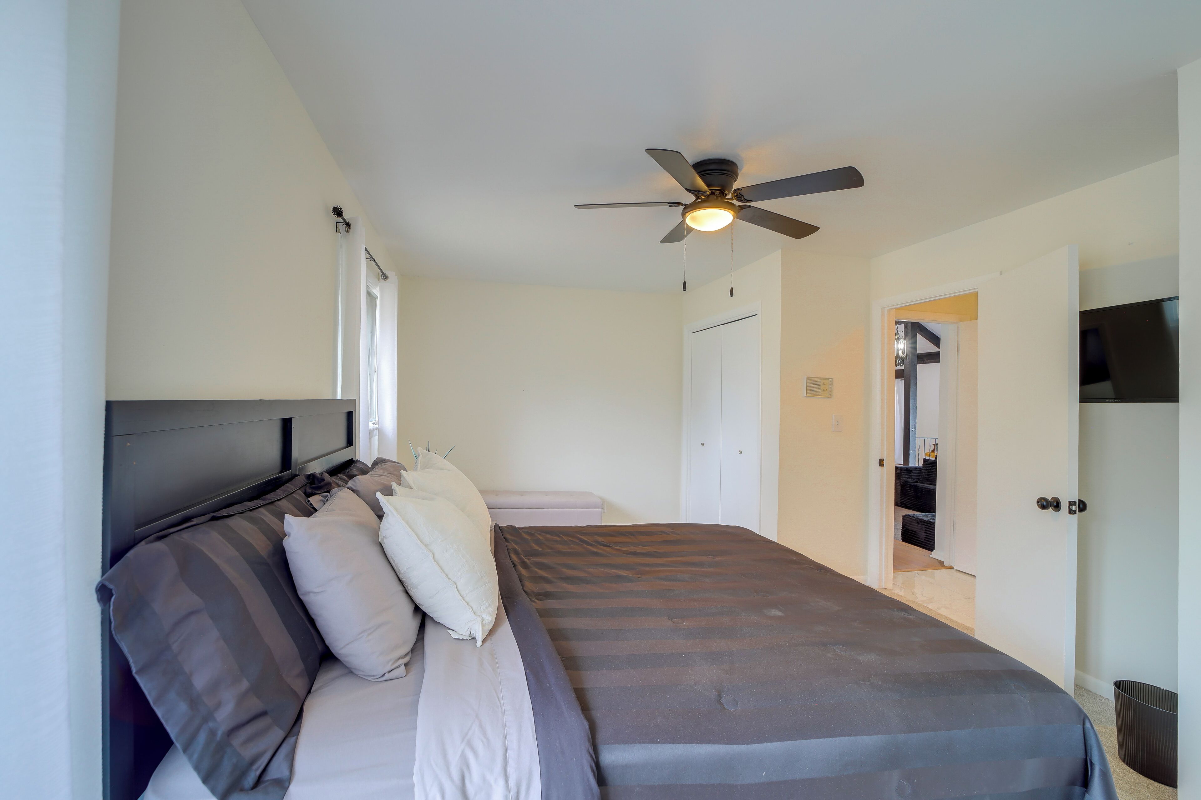 A bedroom with a bed, a ceiling fan, a wardrobe, and a door leading to a staircase.