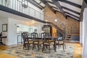 A spacious dining area with a large round table and ornate chairs, a kitchen in the background, and a brick wall with a staircase. - Backyard Oasis! Spacious Tulsa Home w/ Pool (Tulsa)