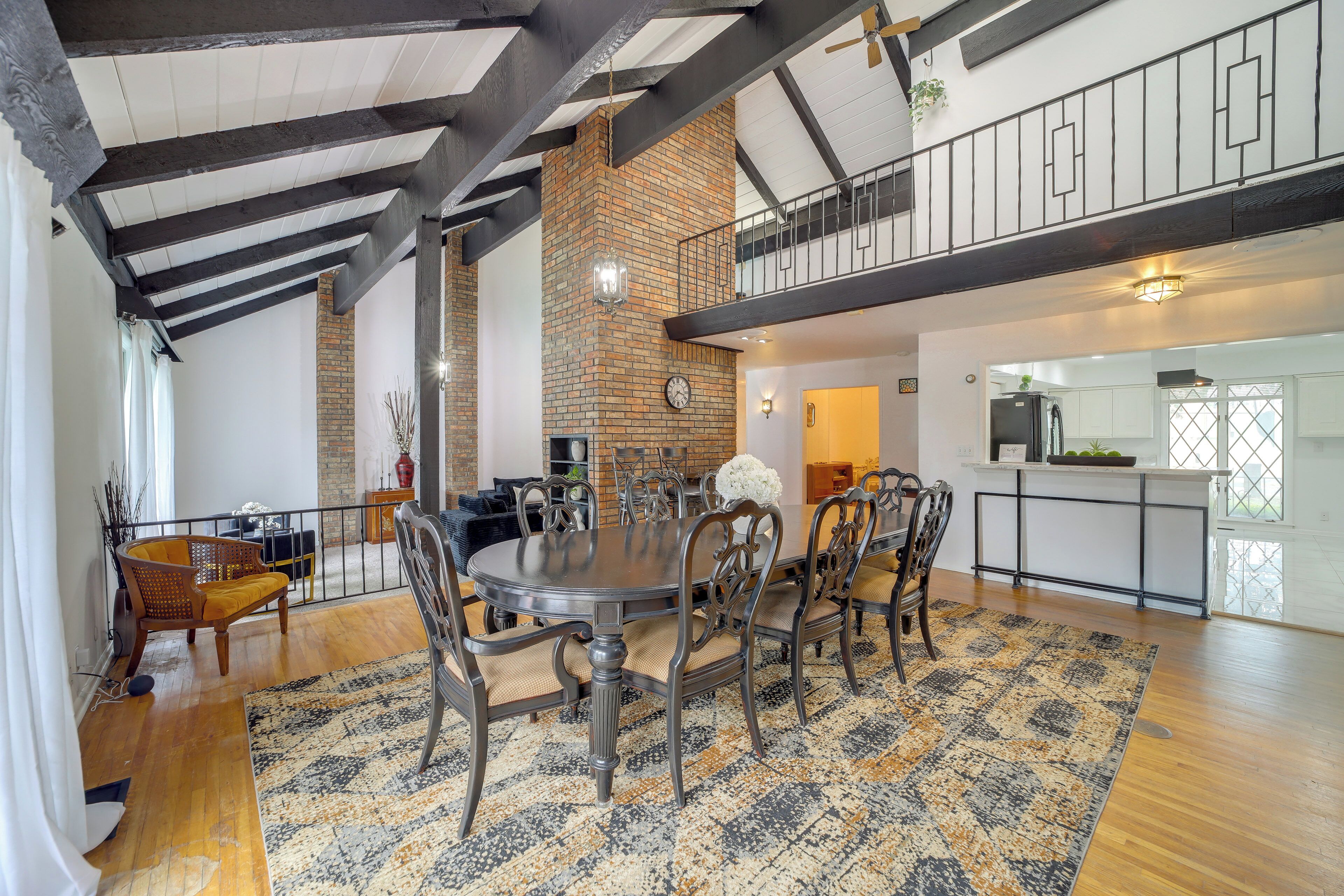 A spacious dining area with a large table and chairs, a brick fireplace, and a balcony with a railing.