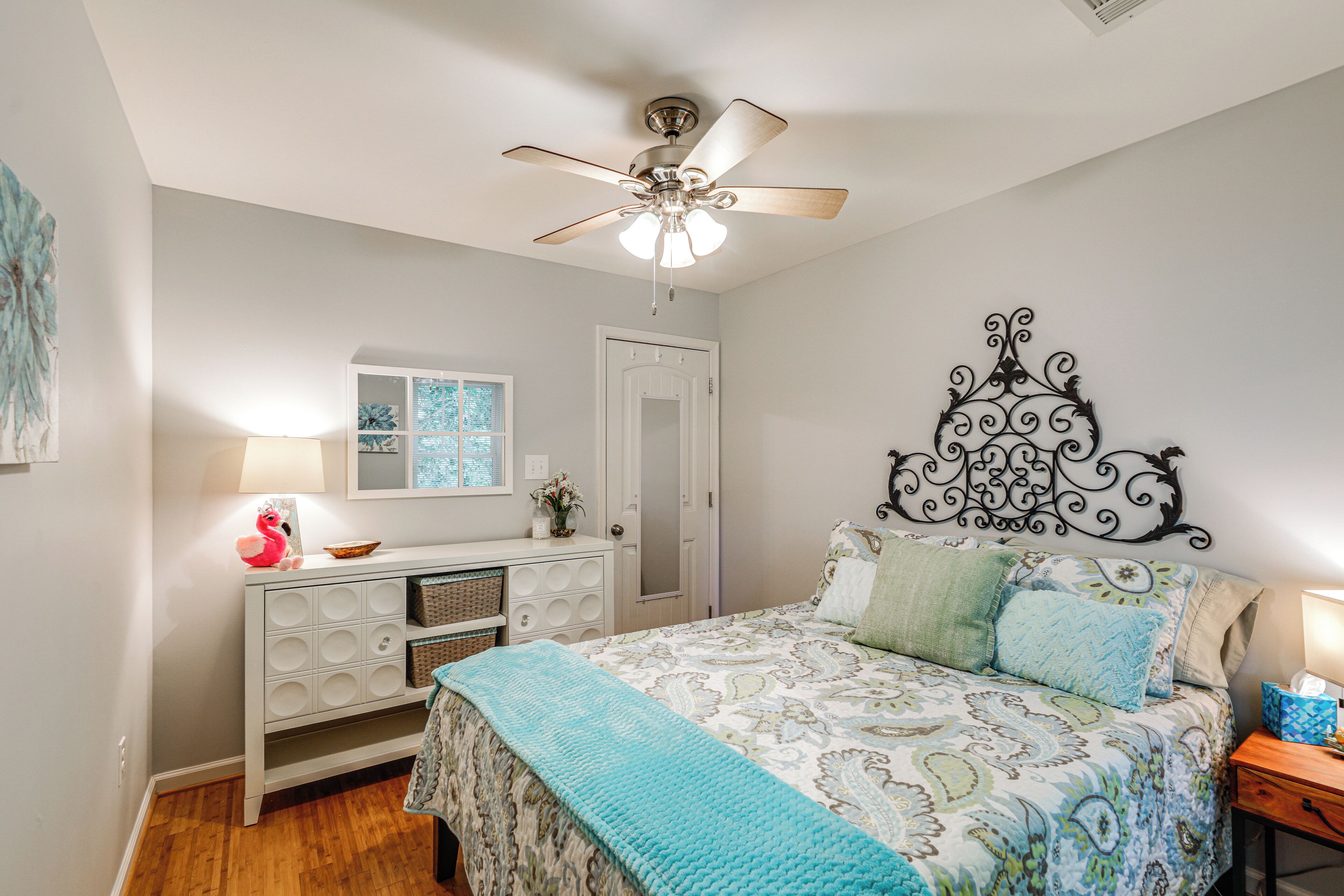 A bedroom with a bed, a dresser, a ceiling fan, a window, and a door.