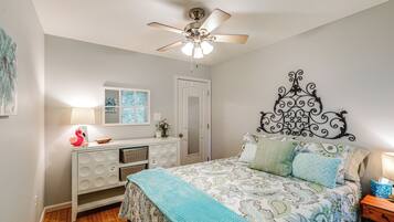 A bedroom with a bed, a dresser, a ceiling fan, a window, and a door.