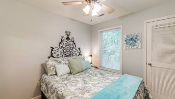 A bedroom with a bed, a ceiling fan, a window with blinds, and a door.