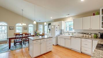 A spacious kitchen with white cabinetry, a dining area with wooden chairs, and a large island with a granite countertop.