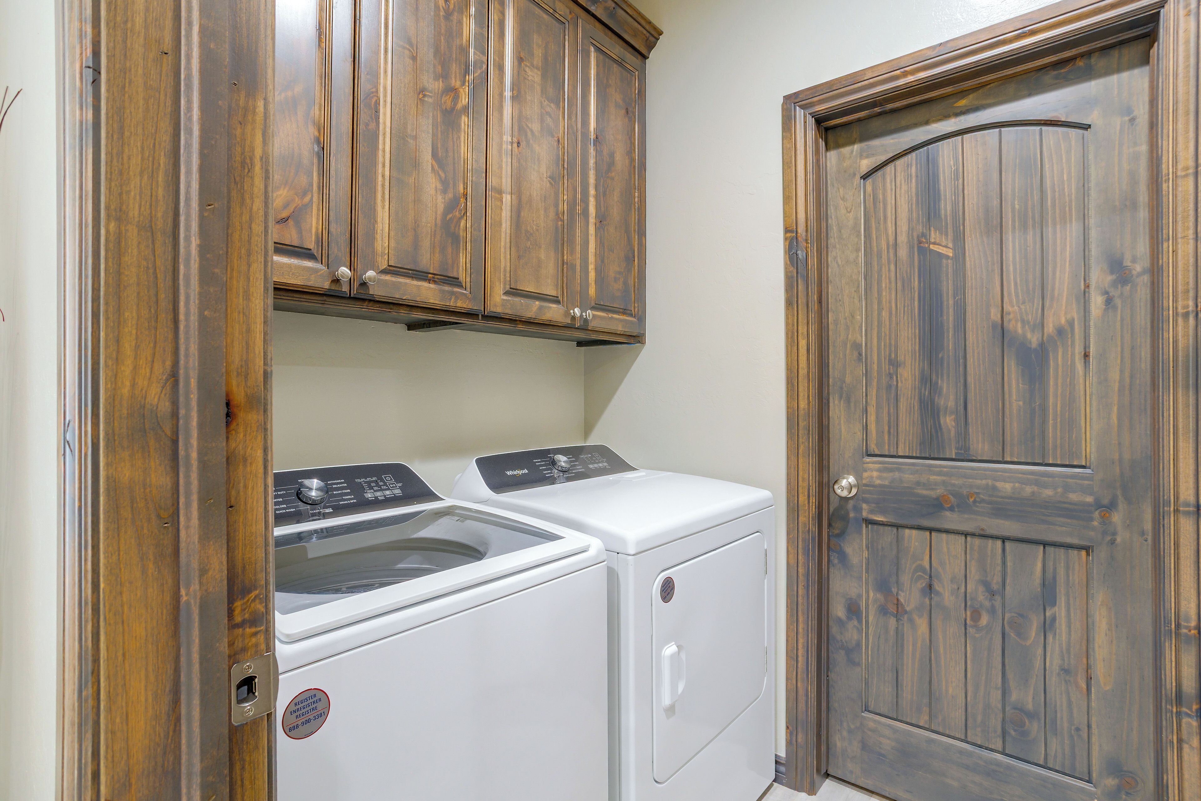 A laundry room with a washer and dryer, wooden cabinets, and a door.