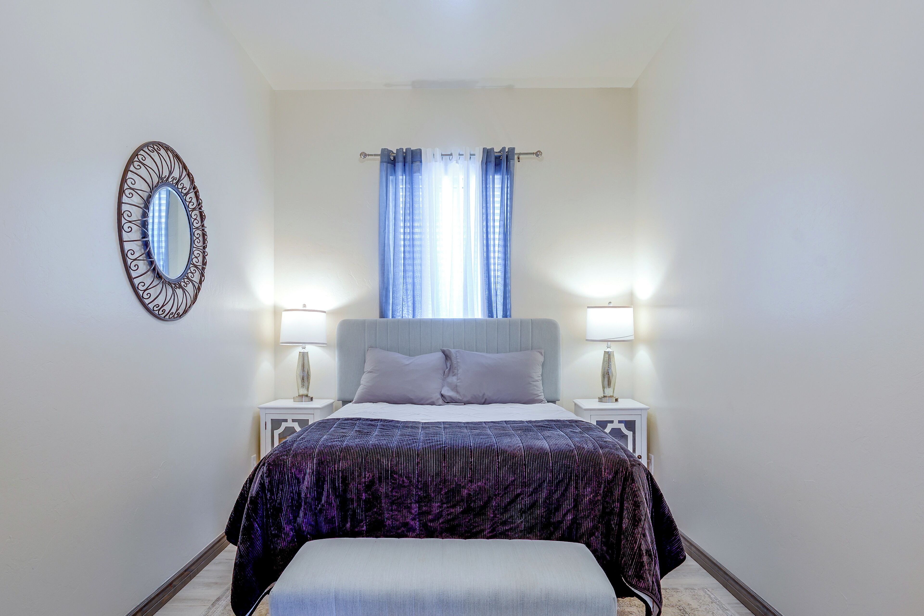 A bedroom with a bed, two bedside tables, a nightstand, a mirror, and a window with curtains.