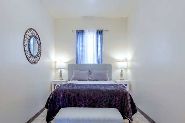 A bedroom with a bed, two bedside tables, a nightstand, a mirror, and a window with curtains.