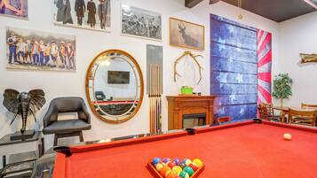 A billiards room with a pool table, a mirror, and various framed pictures on the walls.
