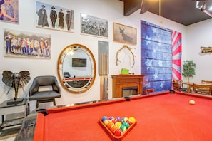 A billiards room with a pool table, a mirror, and various framed pictures on the walls.