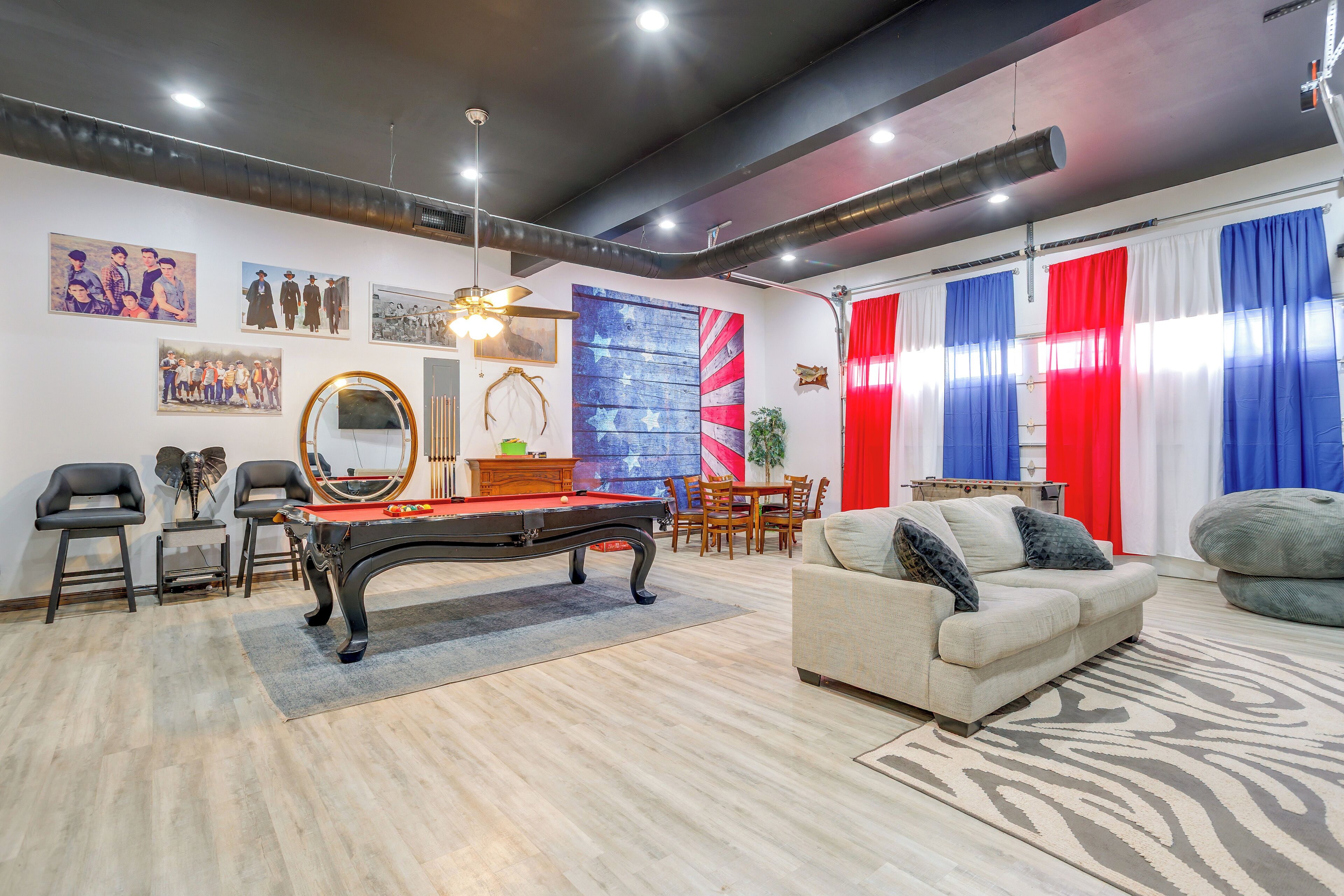A room with a pool table, a sofa, a dining table with chairs, and a red and blue curtain.