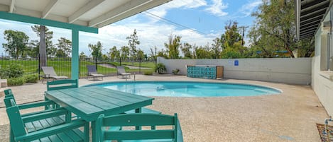 A covered outdoor area with a pool, green seating, and a view of the surrounding landscape.