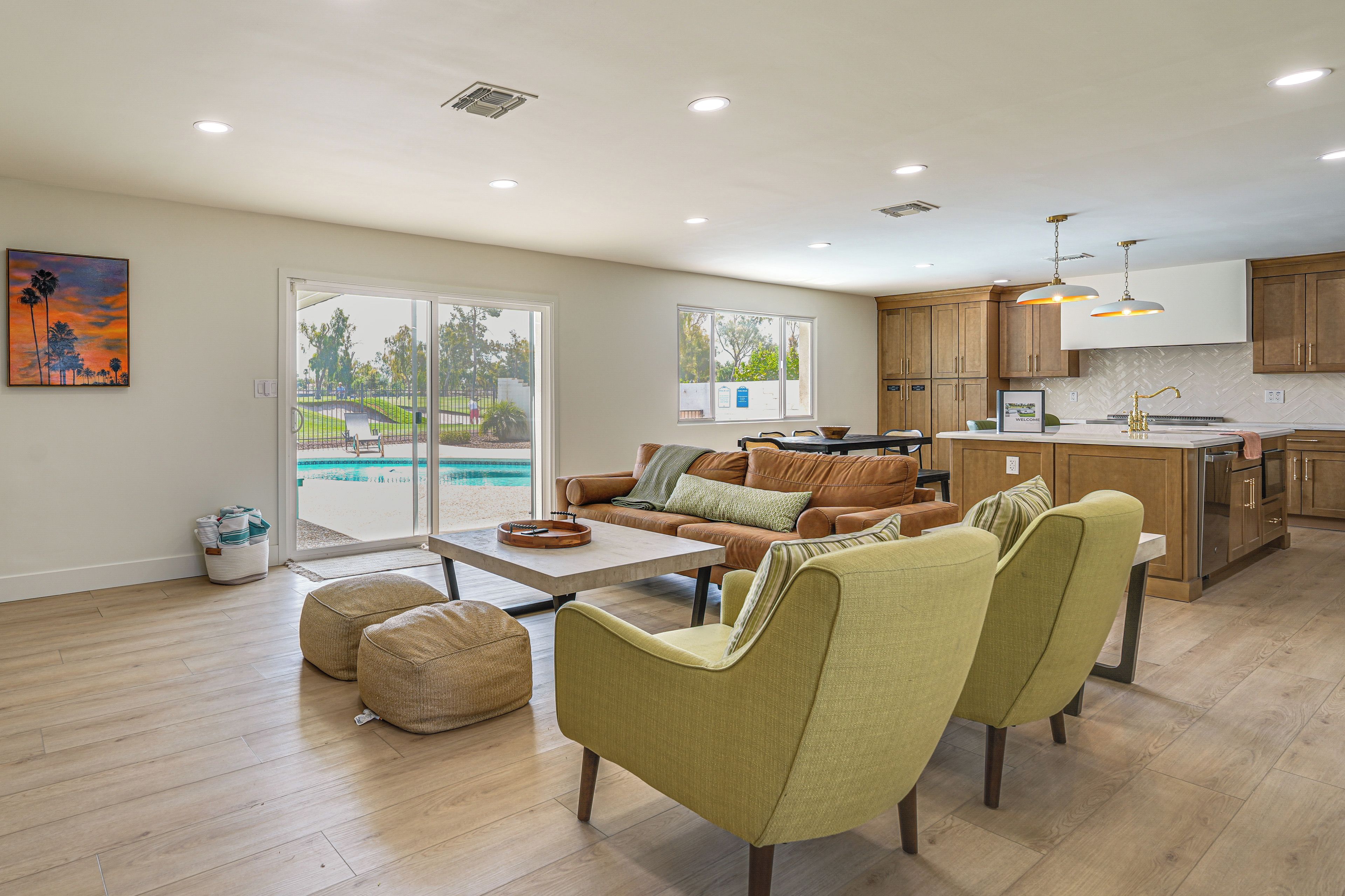 A spacious living area with a pool view, wooden flooring, and a modern kitchen.