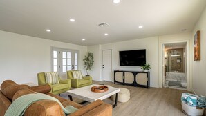 Un salon avec un canapé en cuir marron, un fauteuil vert, une table basse et un téléviseur à écran plat fixé au mur.