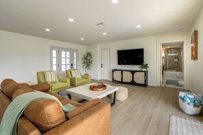 Ein Wohnzimmer mit braunem Ledersofa, einem grünen Sessel, einem Couchtisch und einem flachbildfernseher an der Wand.