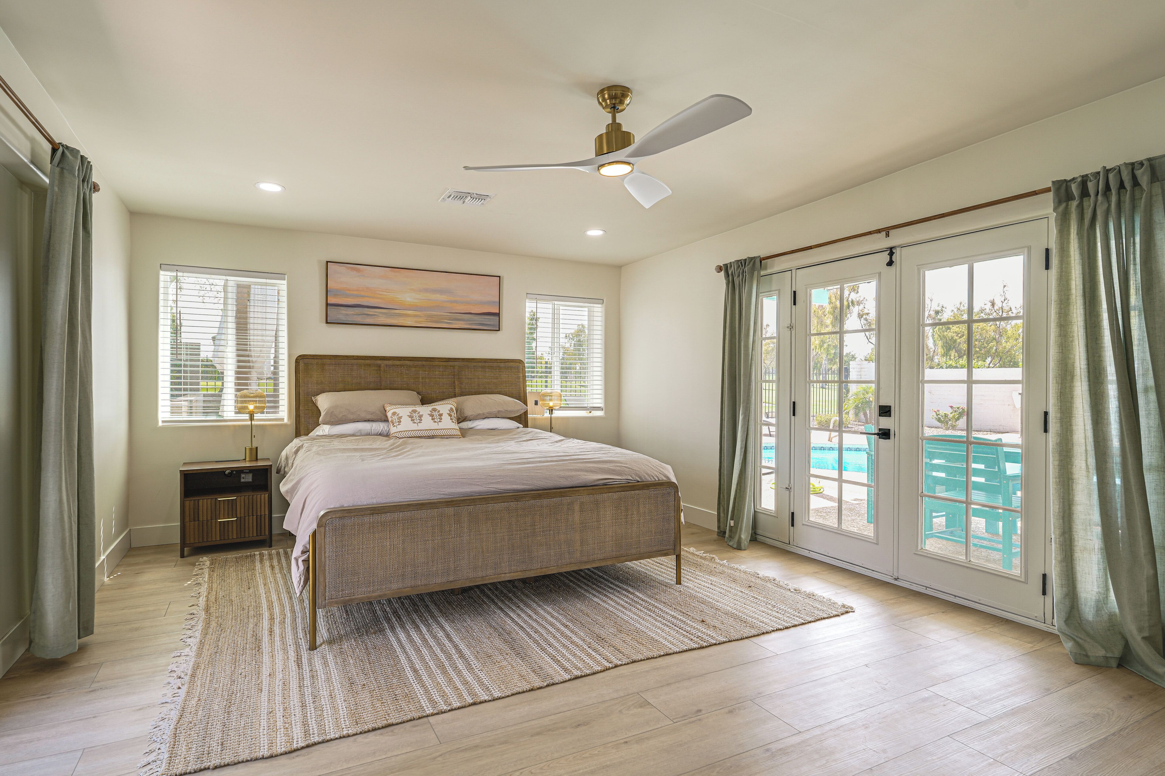 A bedroom with a bed, a nightstand, a ceiling fan, and a view of a swimming pool through the glass doors.