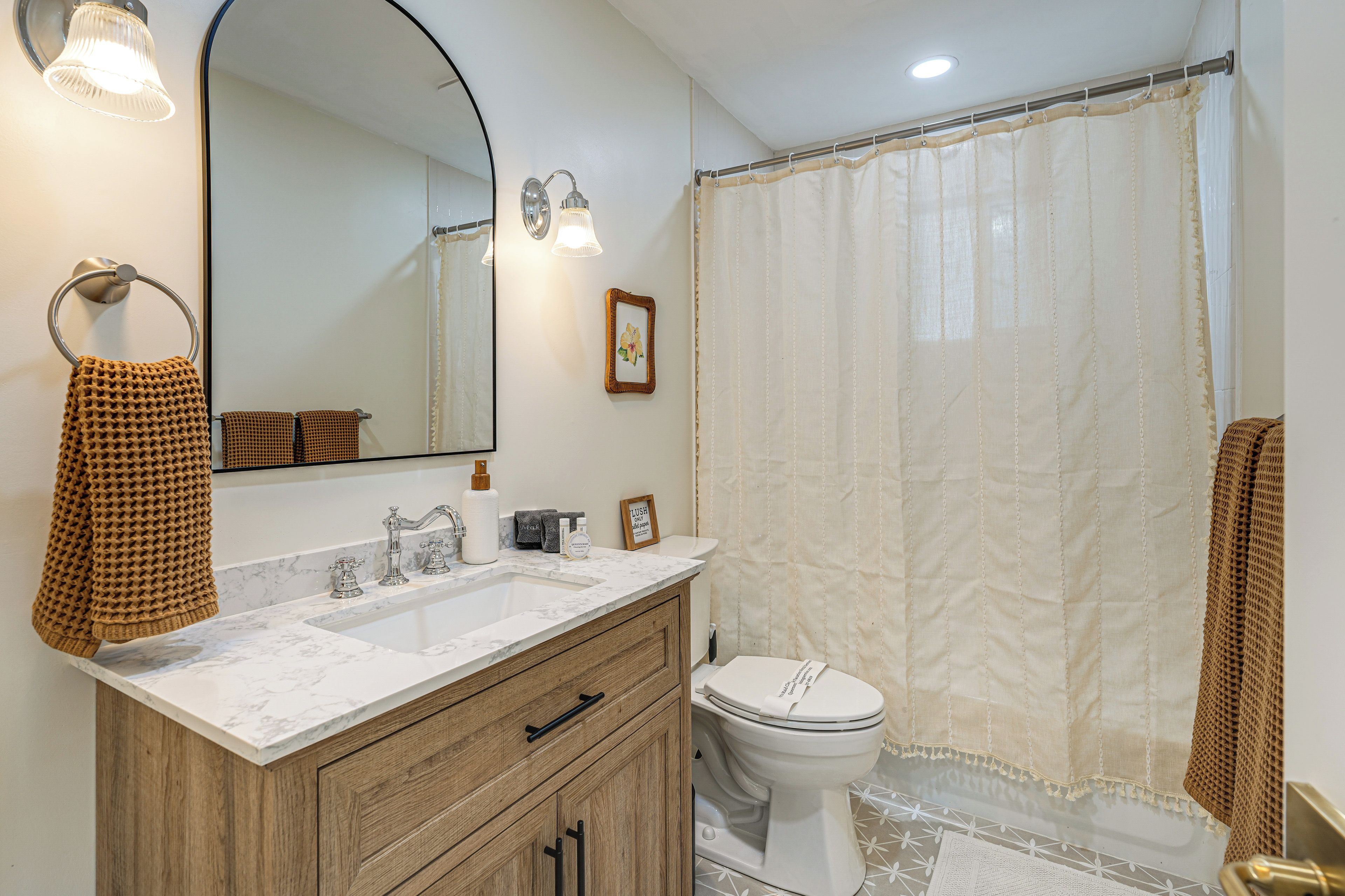 A bathroom with a marble sink, wooden vanity, a toilet, and a shower curtain.