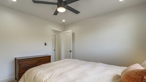 Une chambre à coucher avec un lit, une table de chevet, un ventilateur de plafond et une porte.