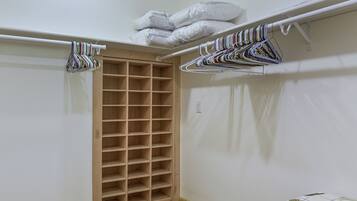 A closet with wooden shelves and hanging space, a light switch, and a door leading to another room.