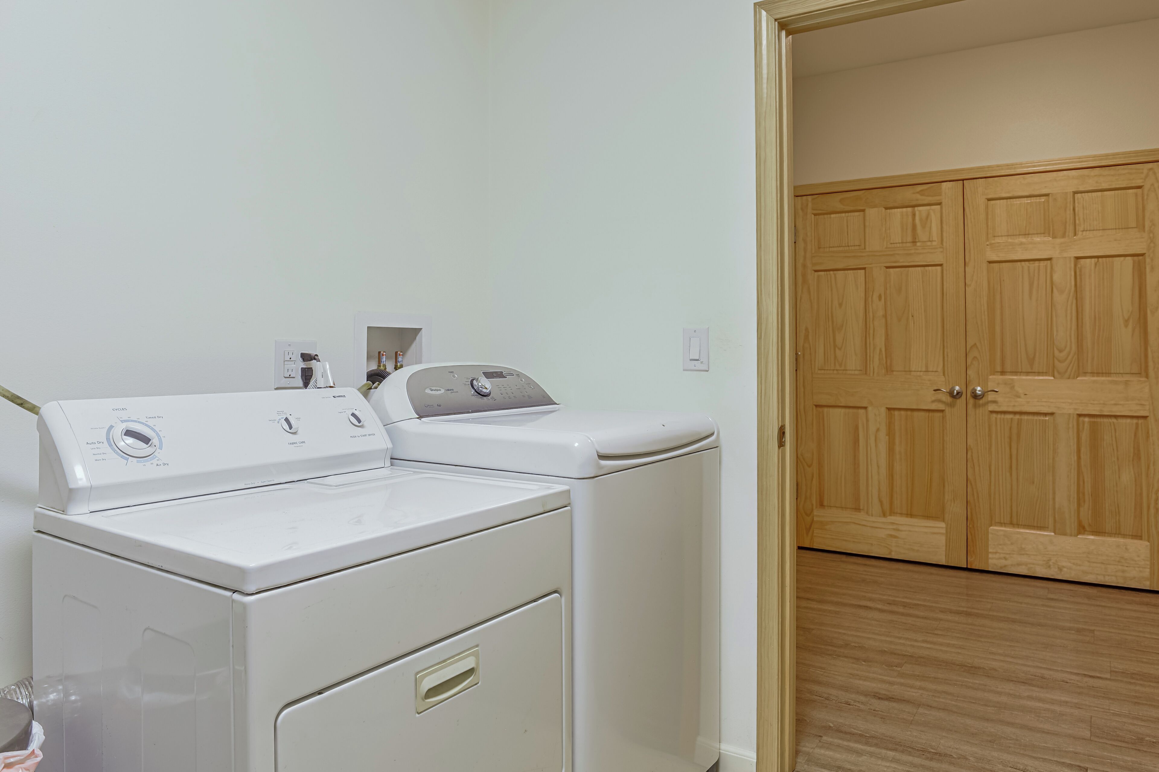 A laundry area with a front-loading washer and dryer, a wooden door, and a light-colored floor.