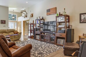 A living room with a brown leather sofa, a patterned rug, a television, and a wooden entertainment center with various items. - Exquisite Private Home Retreat Near Kenai River (Soldotna)