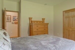 A bedroom with a bed, a wooden dresser, a door, and a wall with framed pictures.