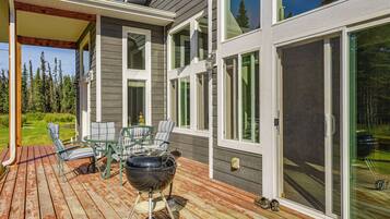 A deck with outdoor furniture and a grill, overlooking a forested area.