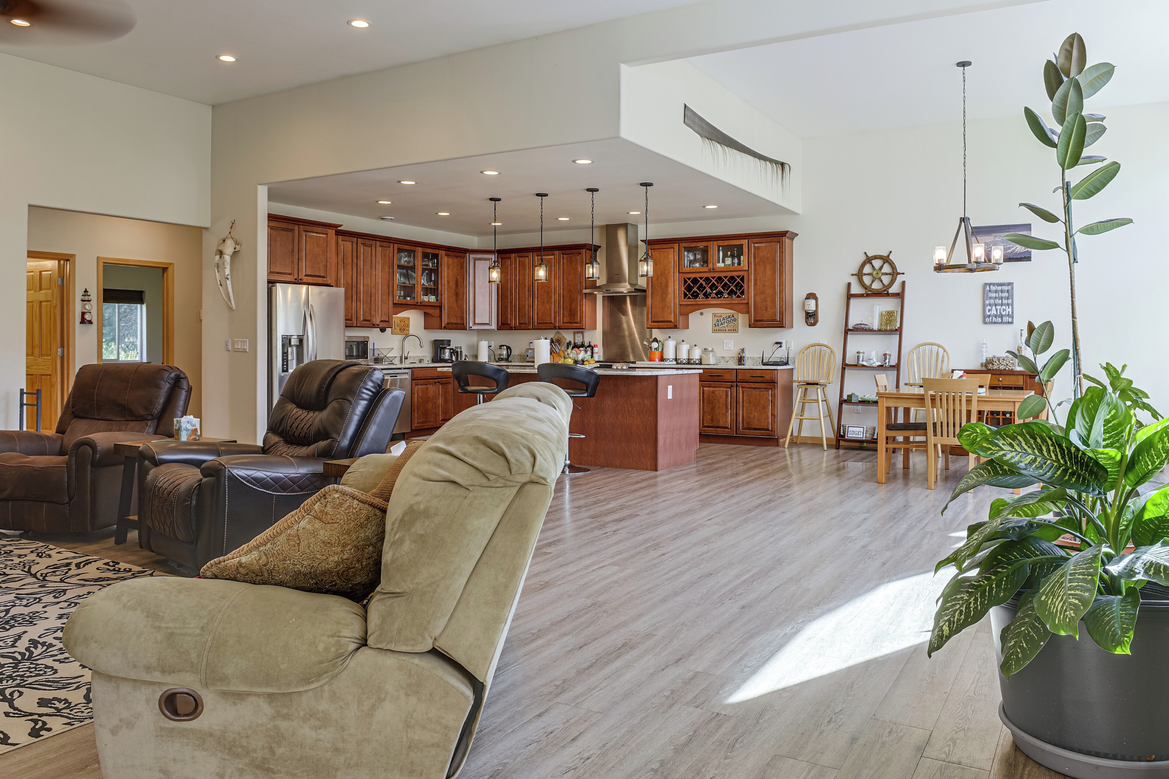 A spacious living room with a leather sofa, a dining area with wooden chairs, and a kitchen with wooden cabinets and stainless steel appliances.