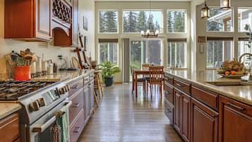 A spacious kitchen with wooden cabinets, a large island, and a view of the forest through the windows.