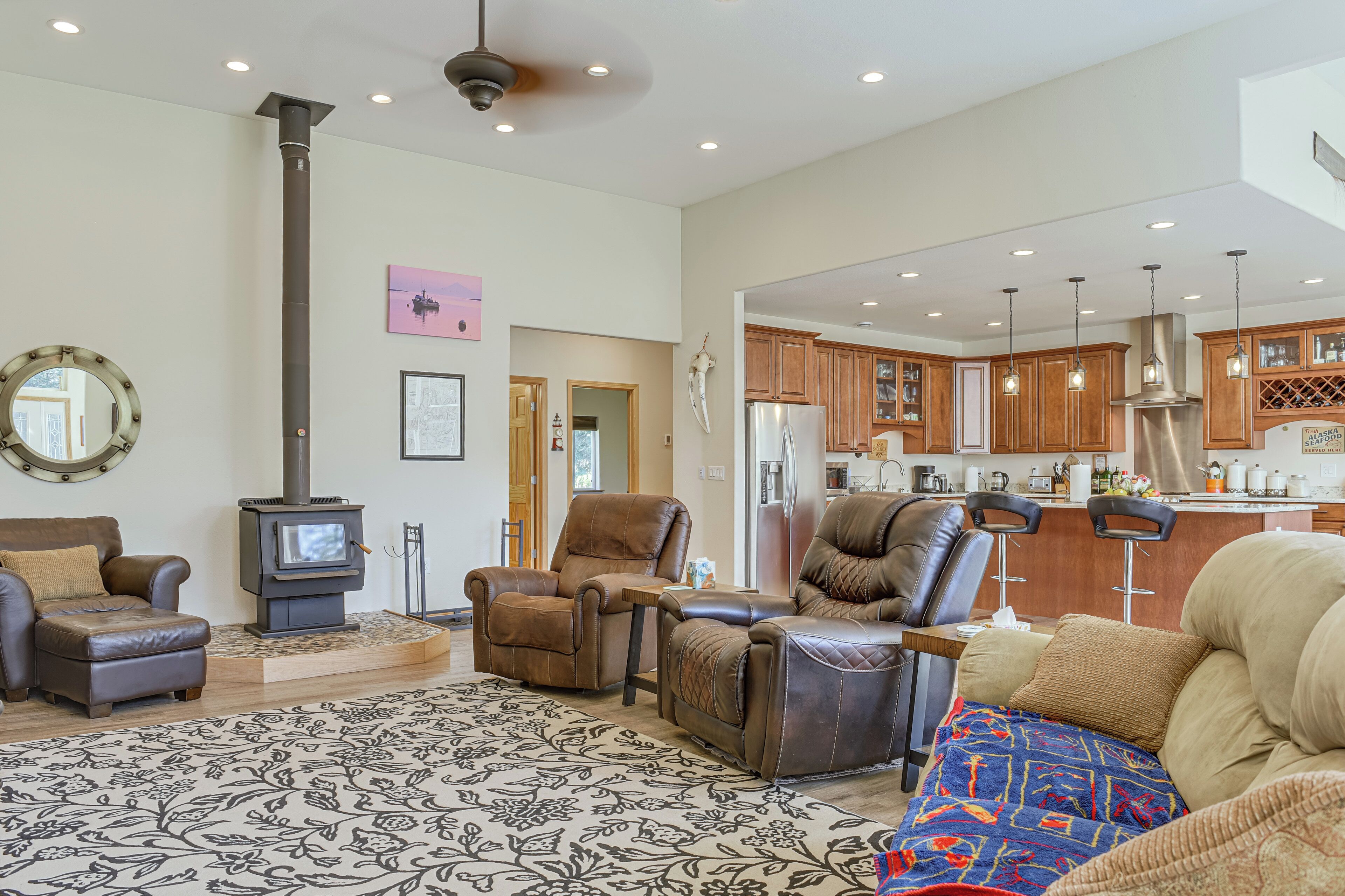 A spacious living room with a fireplace, leather sofas, a patterned rug, and a kitchen in the background.