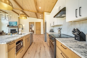 A modern kitchen with wooden cabinets, a marble countertop, and stainless steel appliances. - Brand-new Smokies Cabin w/ Spectacular Mtn Views (Sevierville)
