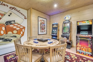 A room with wooden walls, a round wooden table, and various gaming machines including a blackjack and a slot machine. - Brand-new Smokies Cabin w/ Spectacular Mtn Views (Sevierville)