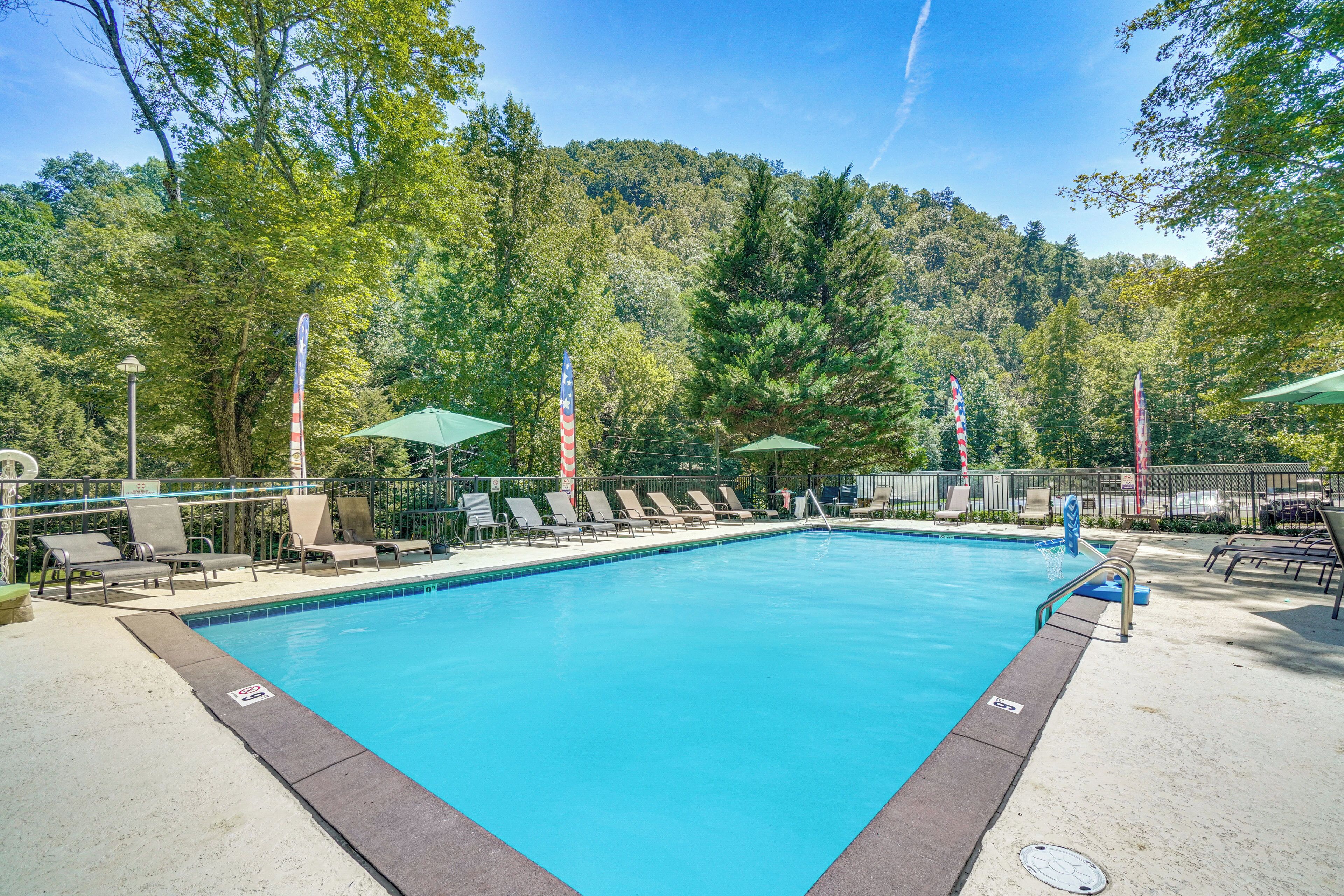 A swimming pool with lounge chairs and umbrellas, surrounded by trees.