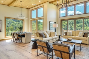 A spacious living area with a high ceiling, large windows, and a dining area with a view of the outdoors. - Brand-new Smokies Cabin w/ Spectacular Mtn Views (Sevierville)