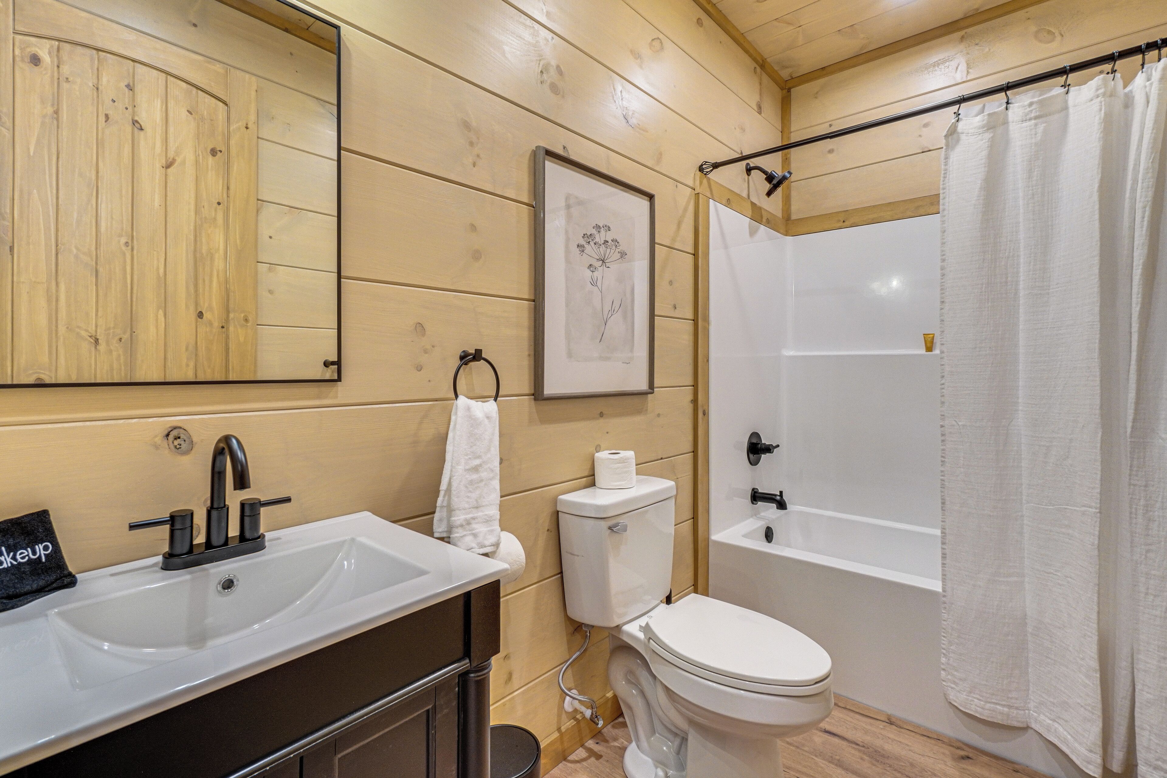 A bathroom with a wooden interior, a white sink, a toilet, a bathtub, and a shower curtain.