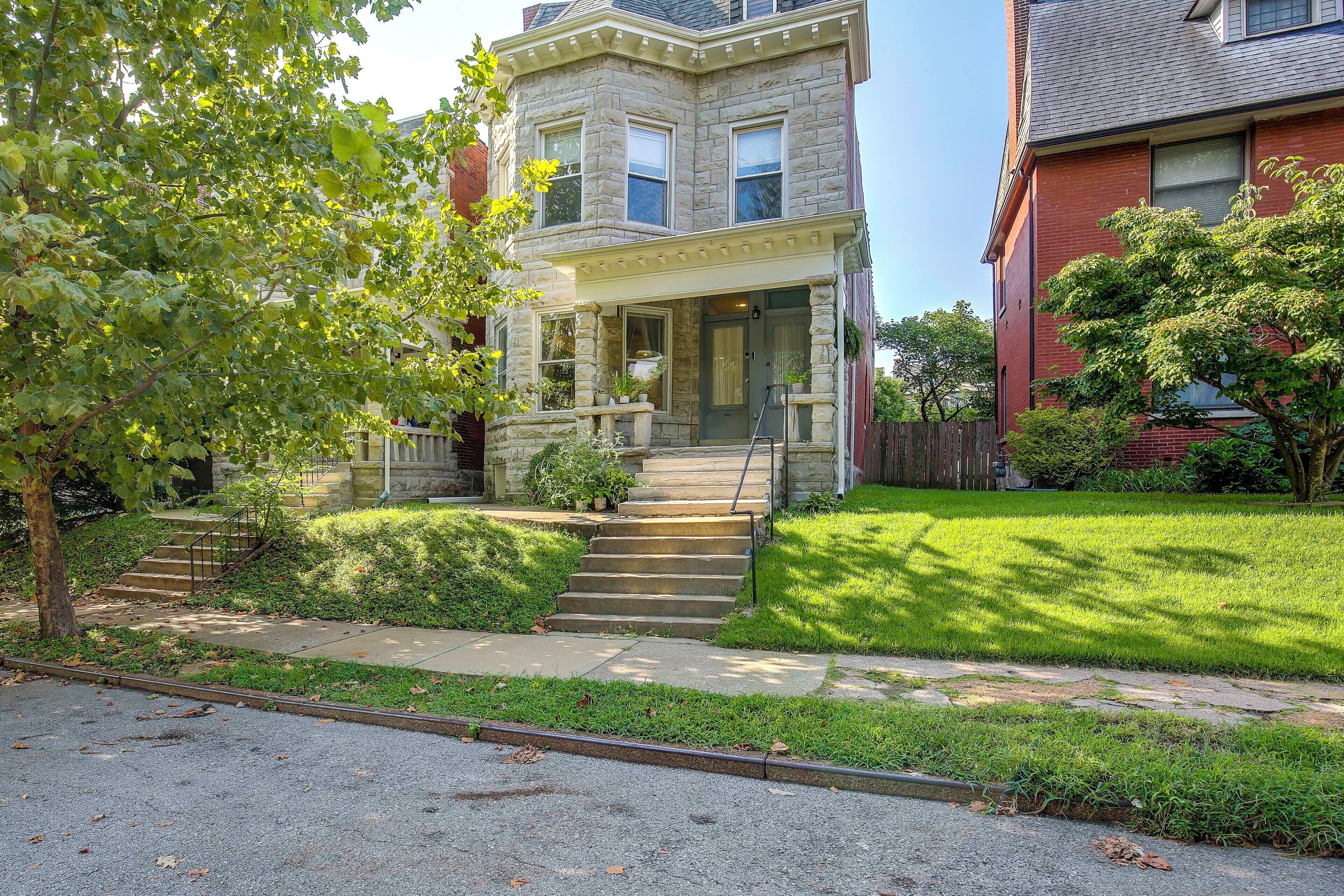A two-story stone house with a front porch, a set of stairs leading to the entrance, and a well-maintained lawn.