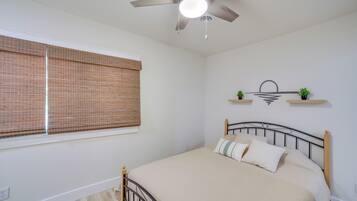 A bedroom with a bed, a ceiling fan, a window with blinds, and wall-mounted shelves with plants.