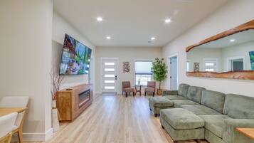 A spacious living room with a large green sofa, a wooden coffee table, and a flat-screen TV mounted on the wall.