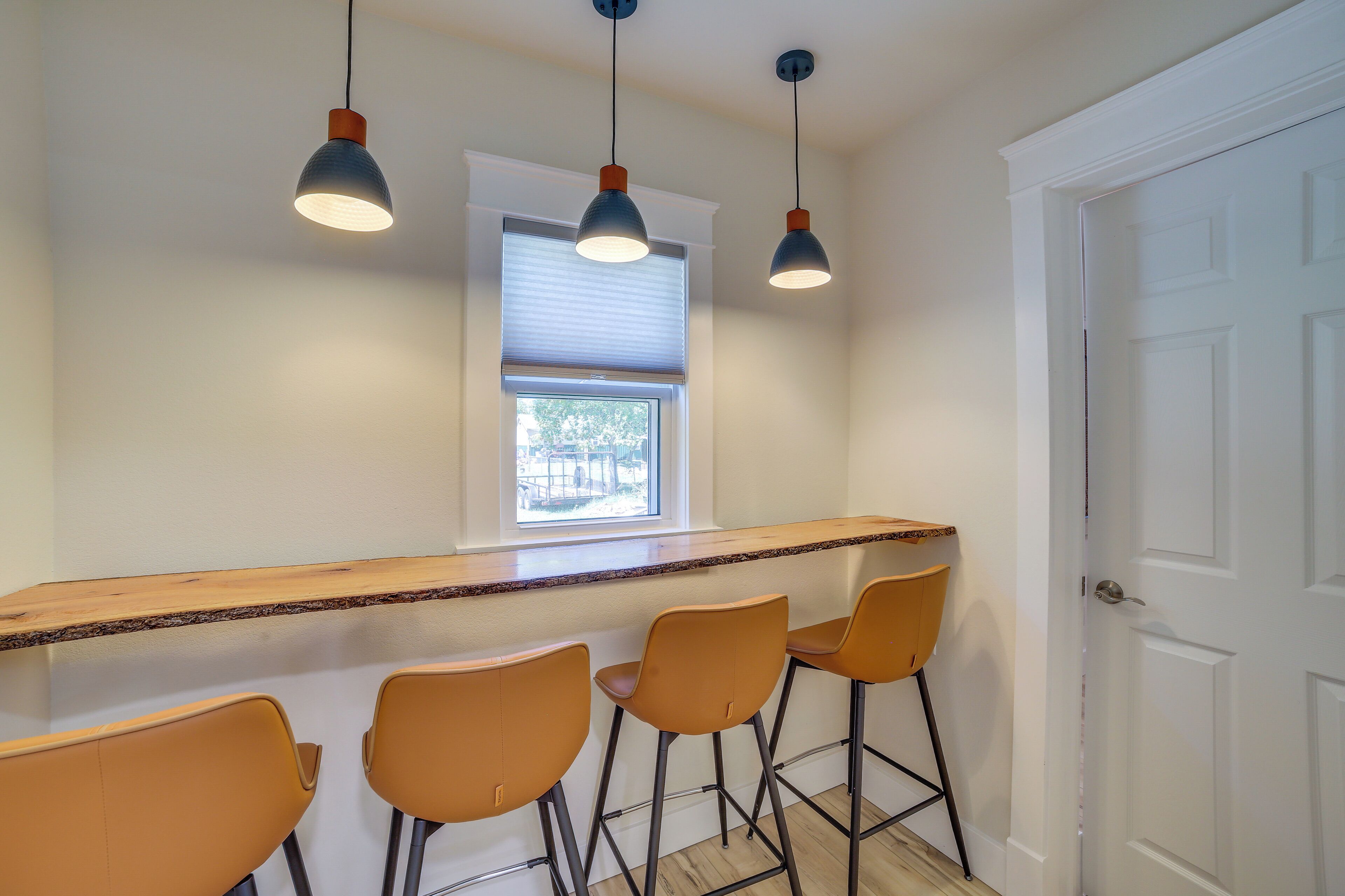 Una cocina con barra, tres taburetes de bar, una ventana con persianas y una puerta.